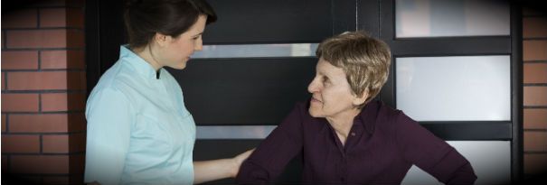 A physician assistant helps an elderly patient out of a clinic. 